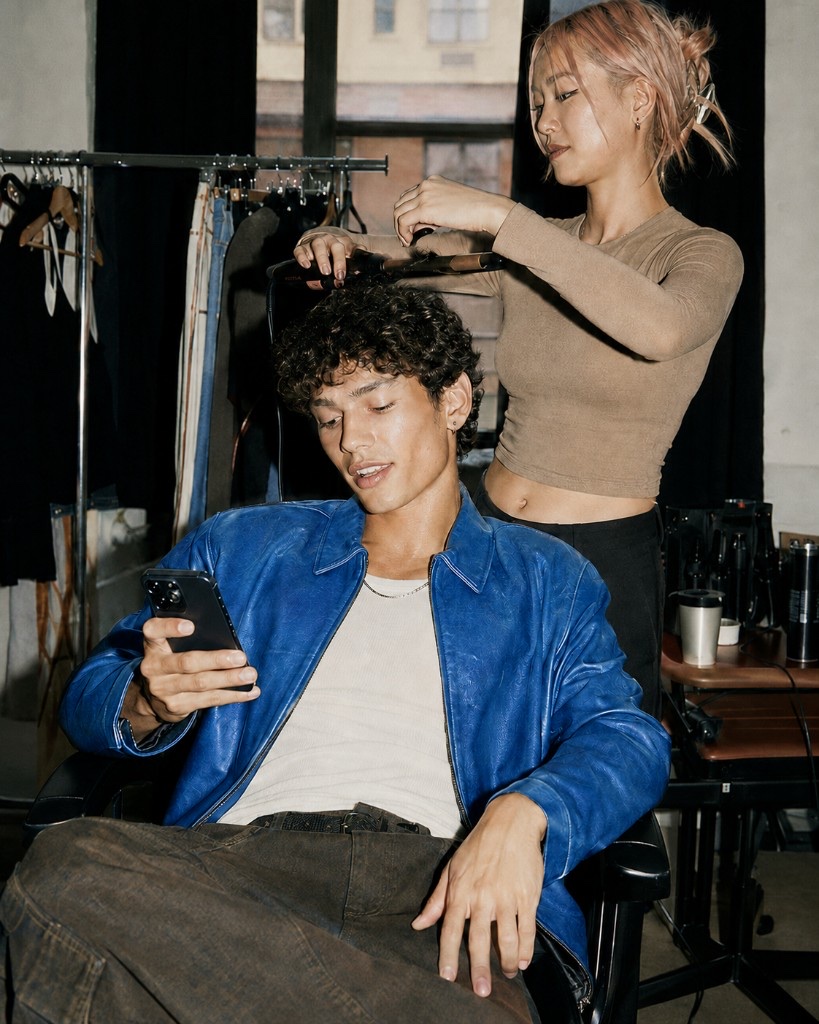 Person in a blue jacket looking at their phone while getting styled