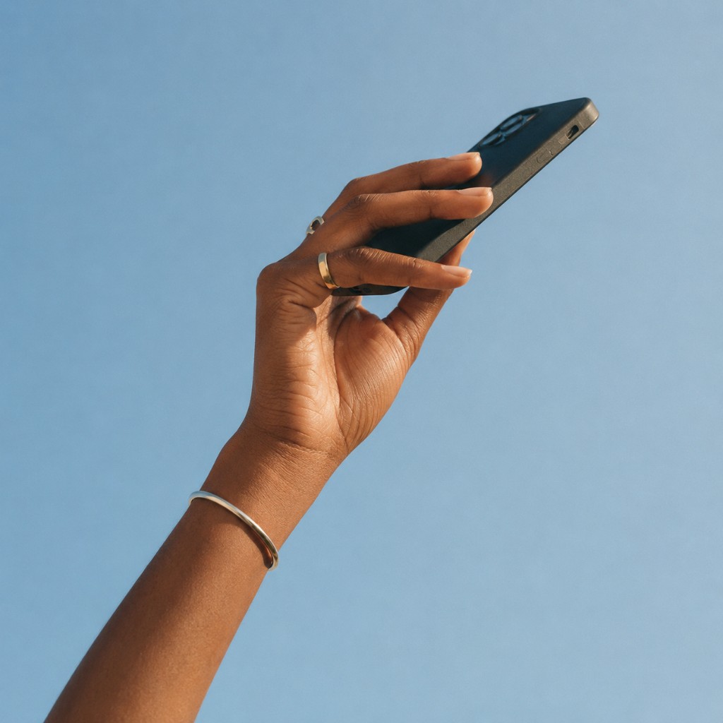 A hand holding a phone against a blue sky